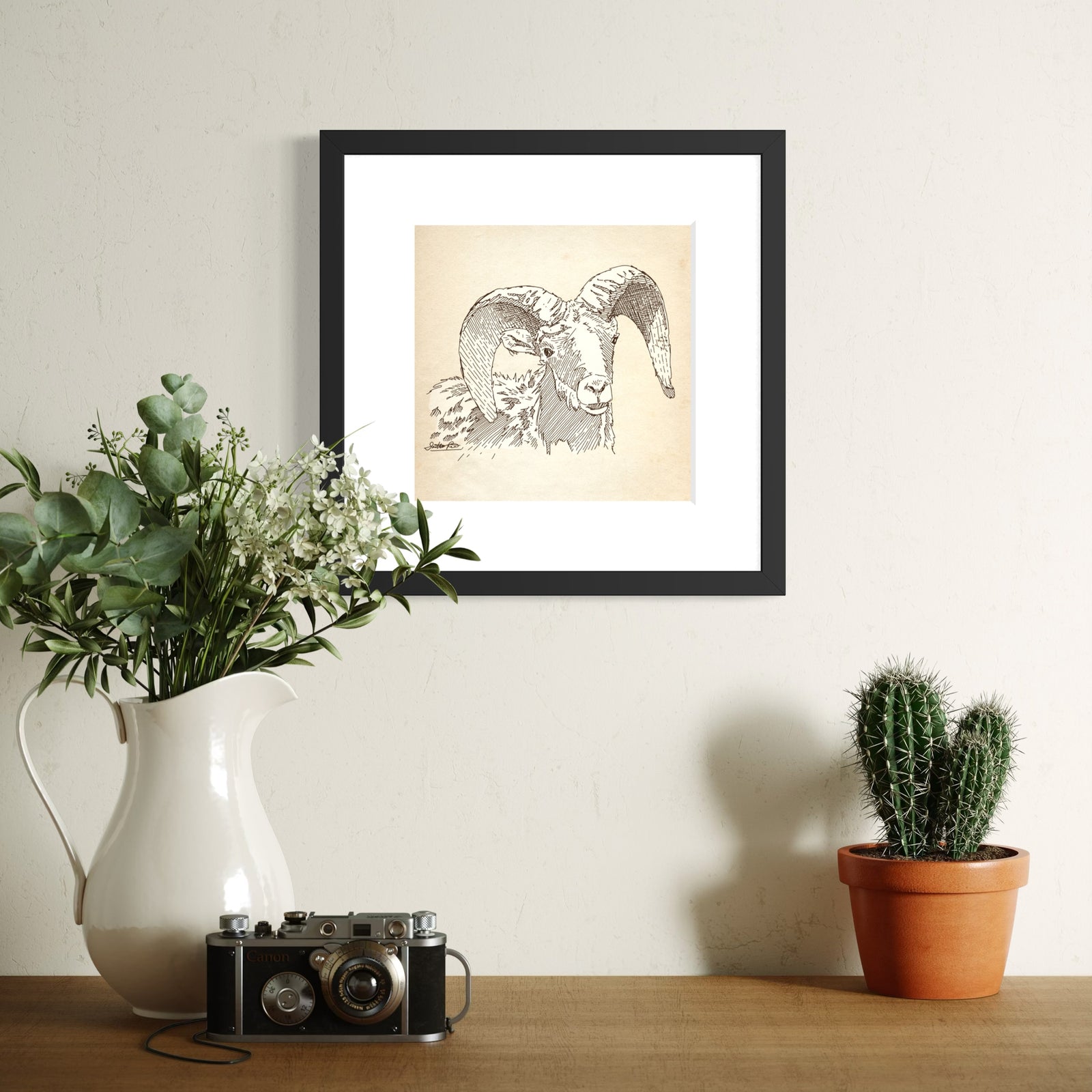 Framed art print featuring a sepia sketch of a ram with large curved horns, set within a white mat and a black frame.