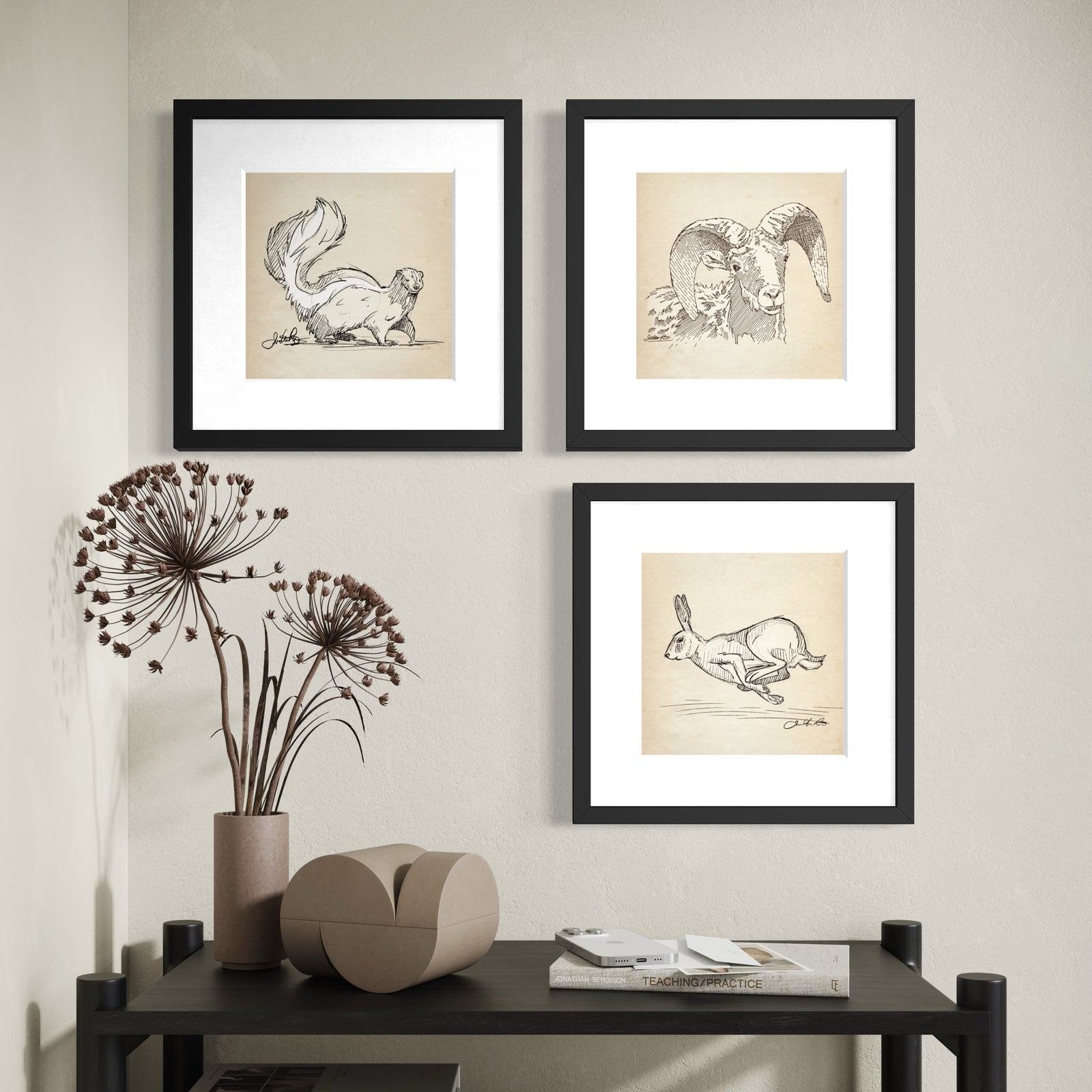 Three framed wildlife sketches of a skunk, bighorn sheep and running rabbit arranged asymmetrically above a black console table.