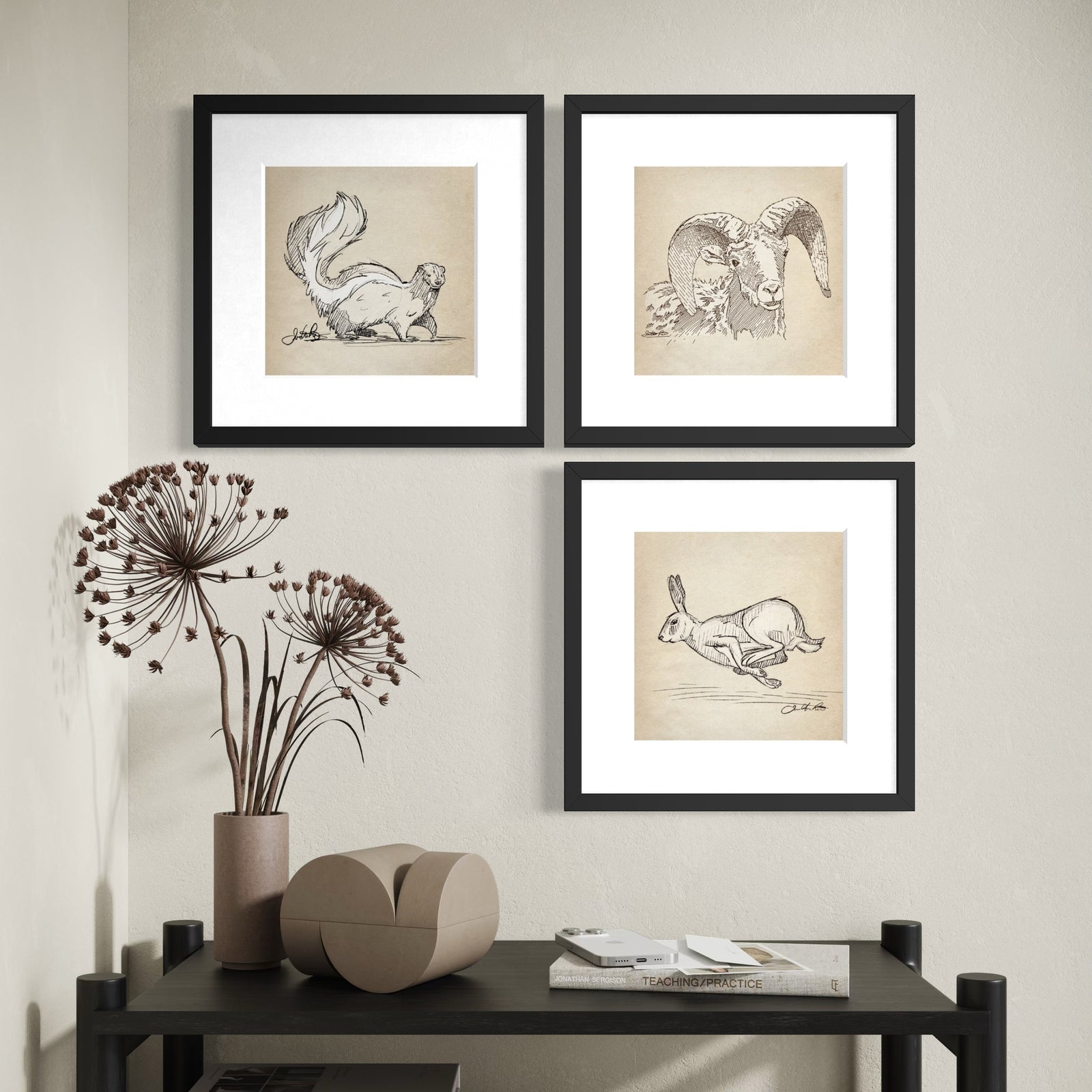 Three framed wildlife sketches of a skunk, bighorn sheep and running rabbit arranged asymmetrically above a black console table.