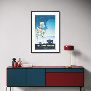 Framed Yellowstone National Park winter poster with bison, snowy landscape, stylized trees, and blue night sky displayed above a modern 
credenza.