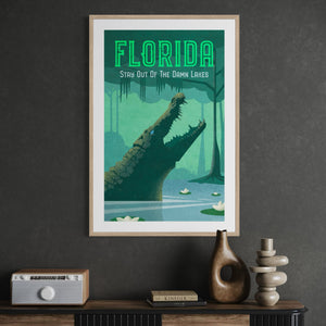 Framed Florida alligator travel poster displayed in an office featuring the humorous “Stay Out of the Damn Lakes” message