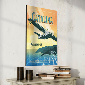 Retro style giclée art print of a PBY Catalina Flying Boat Aircraft flying over Catalina Island, California. It has the words “Visit Catalina Island” at the top. The print’s cool blues and greens combined with the warm sunset sky creates a stunning backdrop for the classic flying boat with bright cool color and yellow highlights. There are additional words a the bottom that says “Everything for your Enjoyment. California Maritime Airlines.”
