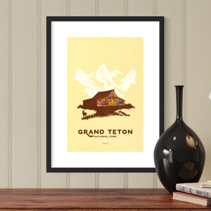 Modern, minimalist giclée art print for Grand Teton National Park in Wyoming. This simple and classy poster depicts the historic T. A. Moulton Barn, with a pronghorn antelope grazing in front and the Grand Tetons behind it.  It has the words “Grand Teton National Park, Wyoming”  at the bottom. The print’s muted overall background color allows the bold and vibrant colors of the main image to pop. 