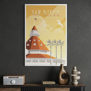 A framed vintage-style travel poster reading 'SAN DIEGO' hangs on a dark gray wall above a console table with decor items. The poster features a warm yellow sky, a terracotta-orange hotel building, palm trees, and white birds.