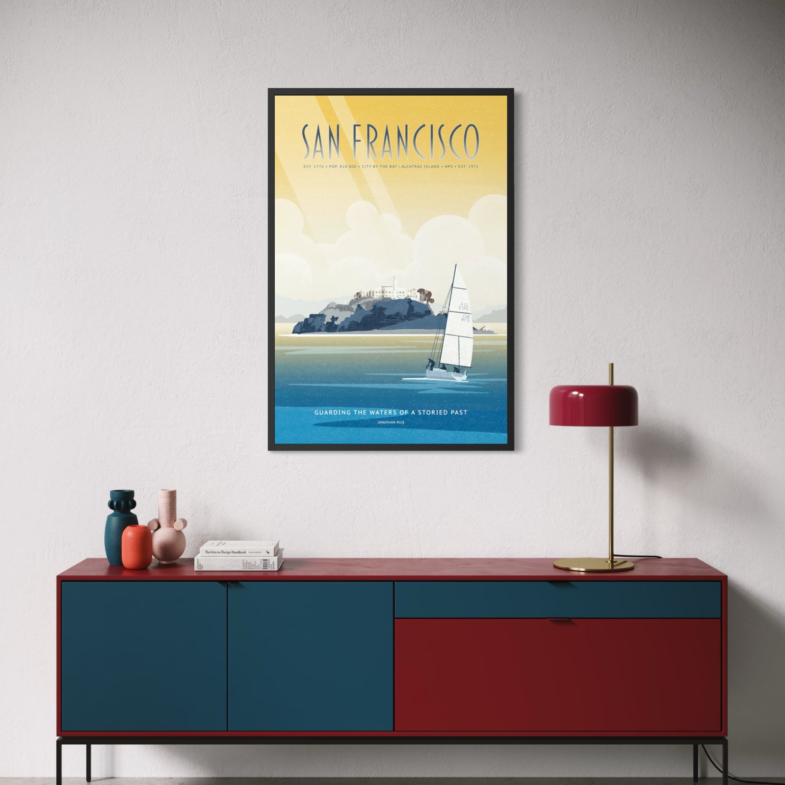 A travel poster for San Francisco featuring a sailboat on blue water with Alcatraz island under a yellow sky. The text reads “SAN FRANCISCO” at the top and “GUARDING THE WATERS OF A STORIED PAST” at the bottom.