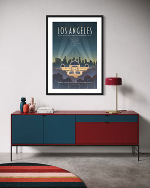 Framed Los Angeles Griffith Observatory poster hanging above a red and navy blue modern credenza with a round striped rug, table lamp, and decorative vases.