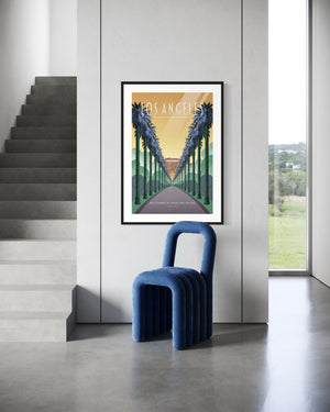 Framed LA palm boulevard poster beside a staircase and blue modern chair in a minimalist interior.