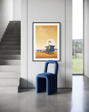 Framed Santa Monica Beach poster on a minimalist wall beside a staircase and modern blue chair.