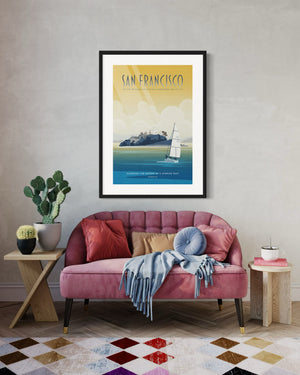 Framed San Francisco Alcatraz poster displayed above a pink tufted loveseat with colorful pillows in a stylish interior.