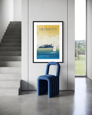 Framed San Francisco Alcatraz poster hanging on a modern concrete wall beside a staircase with a blue sculptural chair.