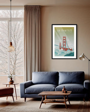 Framed San Francisco Golden Gate Bridge poster hanging above a mid-century modern blue sofa in a warm living room with floor-to-ceiling windows, soft curtains, and a wooden coffee table.