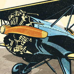 Detail of Retro style giclée art print of a modified WACO Biplane ready for takeoff. It has the words “Adventure in Aviaton” at the top. The print’s dusty yellow sunrise colors combined with bright blues and orange of the plane makes for a stunning image. There are additional words a the bottom that says “Sport biplanes for free spirits. Go Anywhere, Any Time.”.