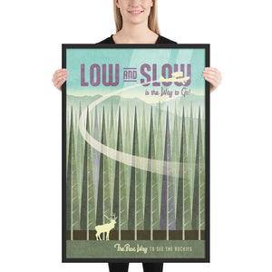 Retro style giclée art print of an elk in a forest in the Rocky Mountains with a plane flying overhead. It has the words “Low and slow is the way to go” at the top. The print’s cool greens and purples combined the glowing sky creates a stunning backdrop for the classic Piper Cub streaking across the scene. There are additional words a the bottom that says “The best way to see the rockies.” Framed size: 24" x 36"