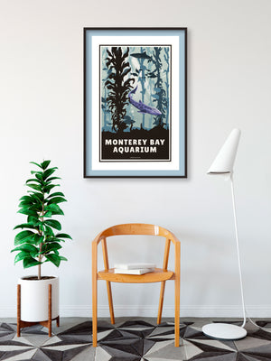 A retro style giclée art print of the Monterey Bay Aquarium in California. It has the words “Monterey Bay Aquarium” on the bottom. The print primarily is in bold aquas and purples with sharks and fish in the kelp forrest exhibit.
